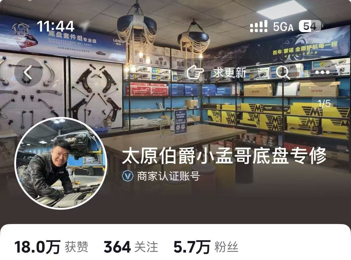 中年男性老板站在汽修店门口,面带微笑,身穿深色夹克,背景是店面招牌和停靠的几辆汽车,阳光明媚