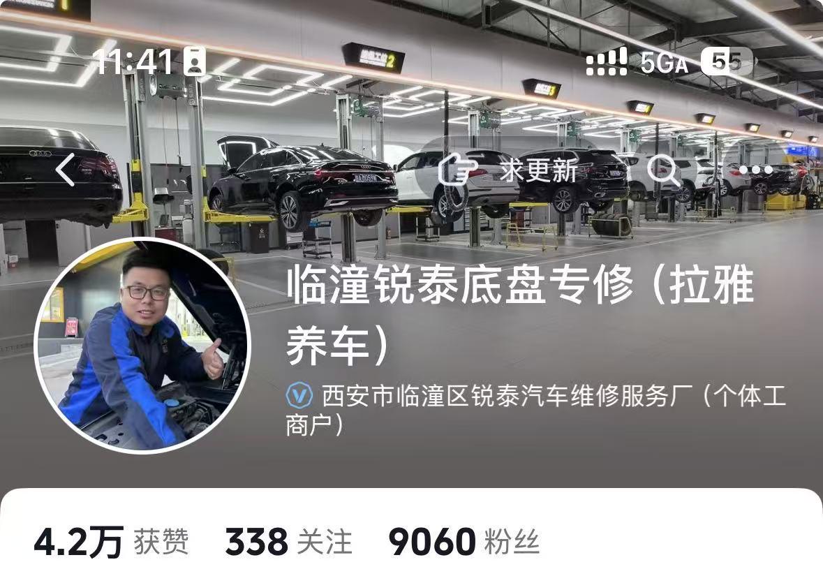汽修店内景,技师正在举升机旁工作,店内光线充足,设备专业,背景有多个停车位和车辆